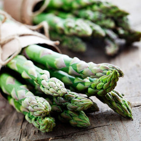 Fresh green asparagus spears with a background of soil, showing healthy, vibrant stalks from Mary Washington seed variety.